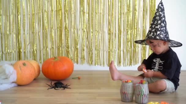 Cute 2 years old boy with magician wizard hat unpack candy sweet near pumpkins — Stock Video