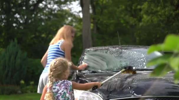 Söt liten flicka med borste hjälpa sin mamma tvätta bil bil bil utomhus. — Stockvideo