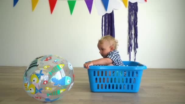 Aktive Jungen sitzen in der Wäschekiste und spielen mit dem großen Ball. Gimbal-Bewegung — Stockvideo