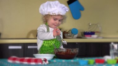 Kız çikolatalı hamuru yeşil önlükle aşçı şapkasıyla karıştırıyor. 4K