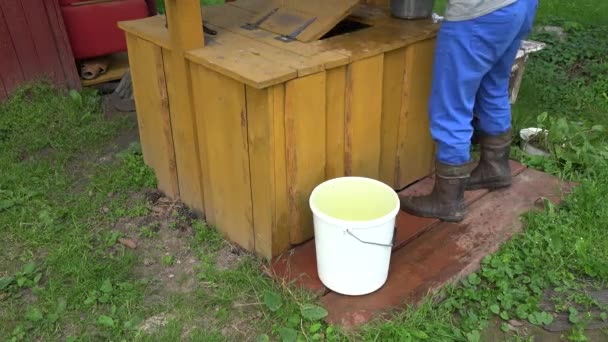 Man tar hinken full med vatten från rustika brunnar i trädgården. 4K — Stockvideo