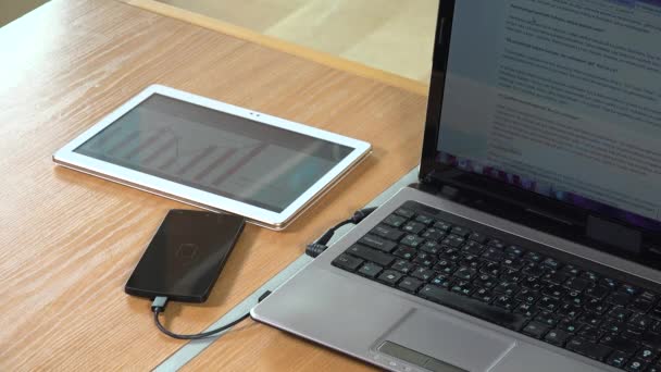 Tableta con gráficos en pantalla, teléfono de carga y computadora portátil — Vídeos de Stock