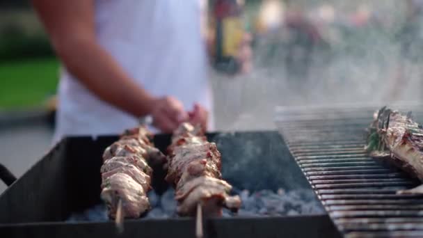 Hombre sosteniendo el volteo de botella escupir con carne de cerdo. Humo procedente de pescado a la parrilla — Vídeo de stock