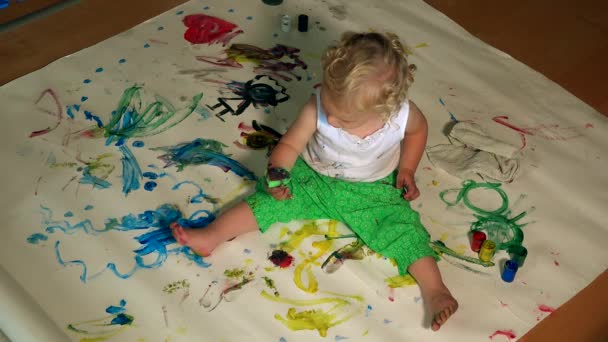 Девушка сидит на бумаге и рисует красочную картину. Детство. 4K — стоковое видео
