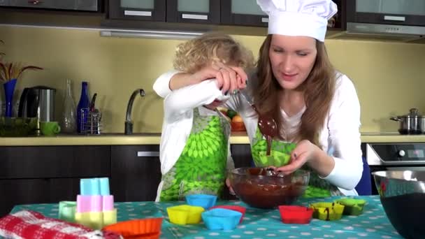 여자 아이들은 엄마가 테이블에서 초콜릿 케이크를 만드는 것을 도와 주면서 재미를 느낍니다. 슬라이드 샷. 4K — 비디오