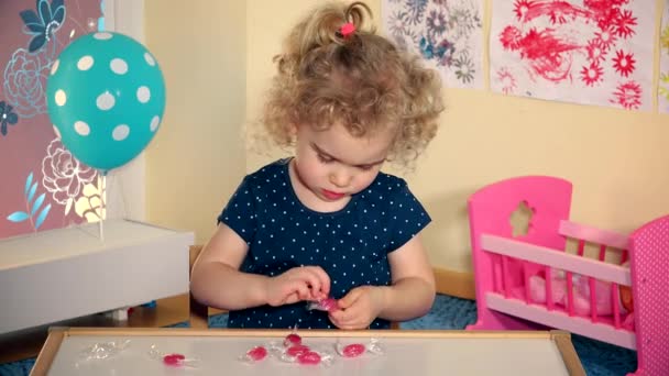 Schattig klein meisje kind pak snoepjes van papier en proef het — Stockvideo