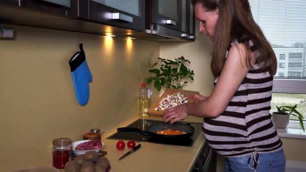 Pregnant woman put cut champion mushrooms into cooking pan on hob — Stock Video