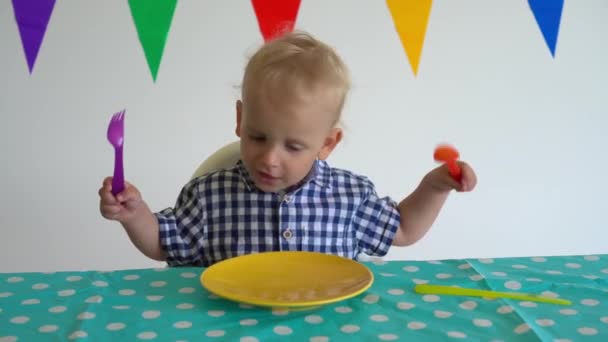 Niño hambriento con tenedor y cuchara sentado en el plato vacío frente. Movimiento del cardán — Vídeos de Stock