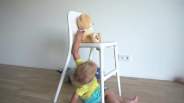 Küçük sarışın bebek oyuncak ayıyla oynuyor. Sandalyenin altında oturuyor. Gimbal hareketi