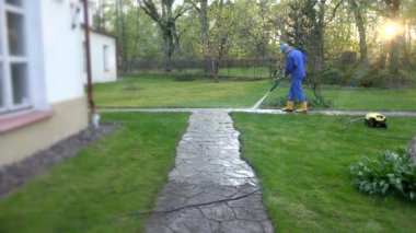 İşçi mavisi giysiler bahçede yüksek basınçlı su püskürtür. 4K