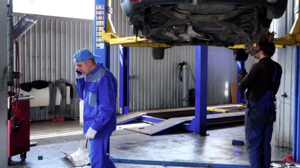 Двое мужчин-механиков работают на ремонте автомобиля на станции технического обслуживания. 4K — стоковое видео