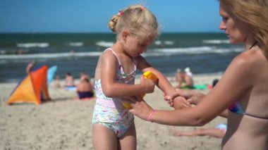 Güzel anne küçük kızının eline güneş kremi sürmesine yardım et.