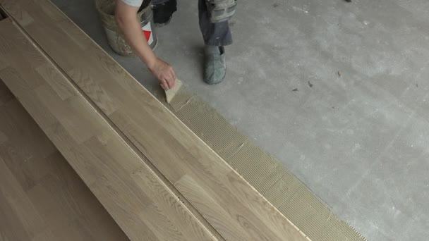 Stolarz z łopatką nakłada klej drzewny na betonową podłogę — Wideo stockowe