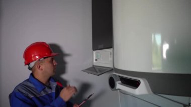Kasklı erkek teknisyen ısıtma kazanının bakımını yapıyor.
