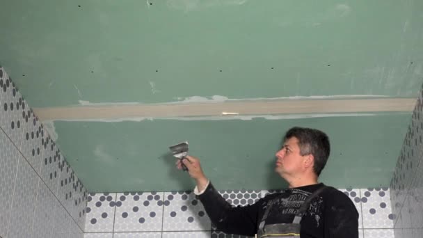 Hombre aplicando compuesto conjunto entre paneles de paneles de yeso y cabezas de tornillo de techo — Vídeo de stock