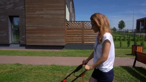 Girl is mowing lawn with electrical lawnmower in house yard. Gimbal movement — Stock Video