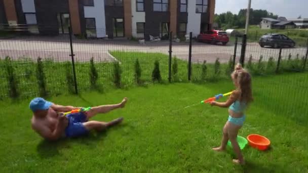 Aktif bir kız çocuğu babasının üzerine oyuncak silahla su sıçratıyor. — Stok video