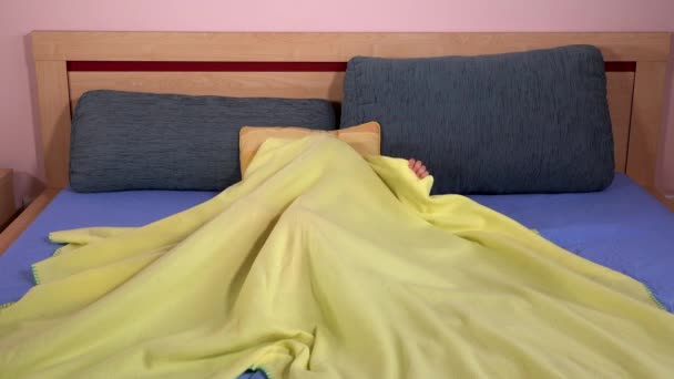 Flickan gömmer sig under gult täcke på sängen. Spel, barndom. 4K — Stockvideo