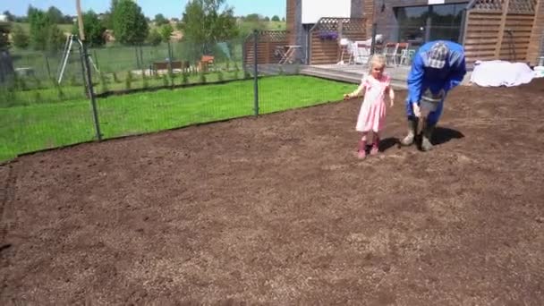 父亲和小助手女儿在院子里播种草坪.手持射击 — 图库视频影像