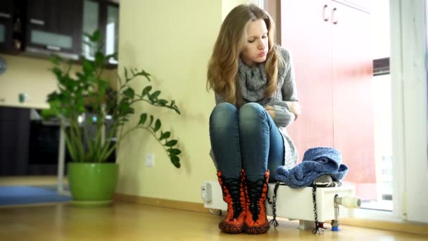Femme assise sur le radiateur gelé à la maison et mettre un chapeau et une écharpe. 4K — Video