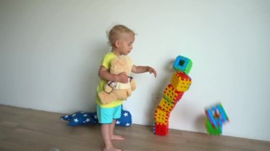 Oyuncak ayıyı tutan yaramaz çocuk renkli bloklardan yapılmış kuleyi yıktı.