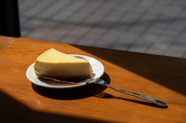 Dilimlenmiş New York Cheesecake beyaz tabakta ahşap arka planda