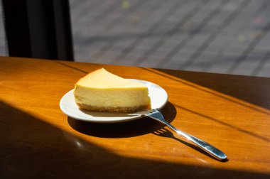 Dilimlenmiş New York Cheesecake beyaz tabakta ahşap arka planda
