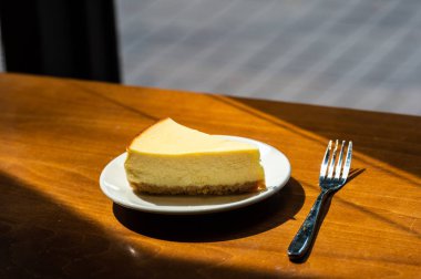 Dilimlenmiş New York Cheesecake beyaz tabakta ahşap arka planda