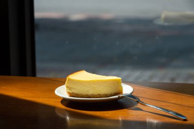 Dilimlenmiş New York Cheesecake beyaz tabakta ahşap arka planda