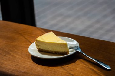Dilimlenmiş New York Cheesecake beyaz tabakta ahşap arka planda