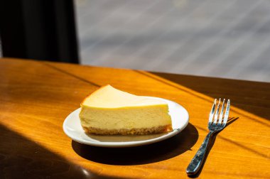 Dilimlenmiş New York Cheesecake beyaz tabakta ahşap arka planda