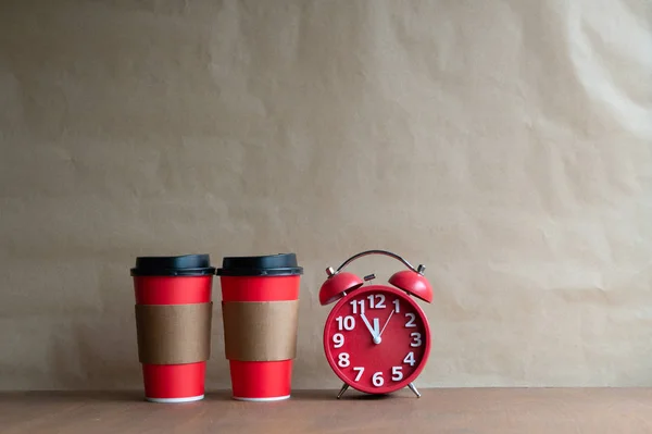 Coffee time concept - two disposable coffee cups and retro alarm clock on white background with copy space