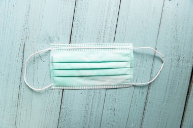 Ahşap masa arkasında tıbbi yüz maskesi, tahta arka planda yeşil yüz maskesi seçici odak.