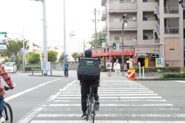 Osaka, Japonya - Ekim 2019: Uber Eats bisikletçisi Roppongi caddesinde bisiklet sürüyor