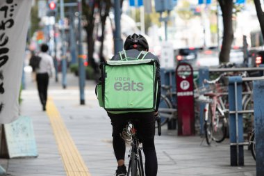 Osaka, Japonya - Ekim 2019: Uber Eats bisikletçisi Roppongi caddesinde bisiklet sürüyor