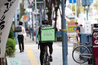 Osaka, Japonya - Ekim 2019: Uber Eats bisikletçisi Roppongi caddesinde bisiklet sürüyor