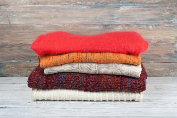 Knitted wool sweaters. Pile of knitted winter clothes on wooden background, sweaters, knitwear, space for text