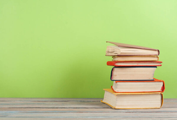 Book stacking. Open hardback books on wooden table and green background. Back to school. Copy space for ad text.