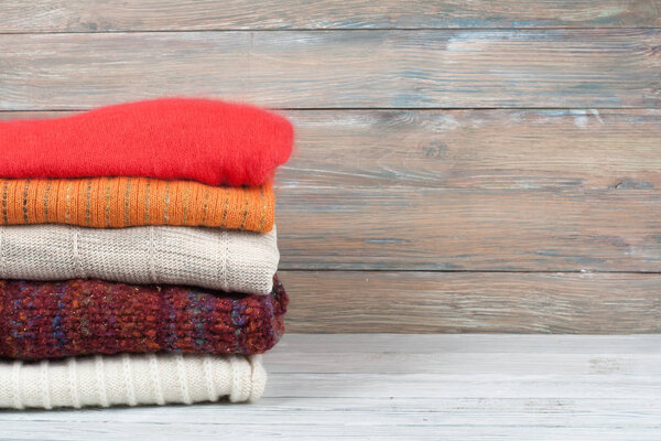 Knitted wool sweaters. Pile of knitted winter clothes on wooden background, sweaters, knitwear, space for text