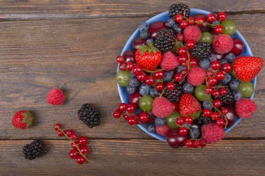 Bir kase rustik ahşap masa üzerinde çeşitli yaz taze çilek. Antioksidan, detoks diyet, organik meyve