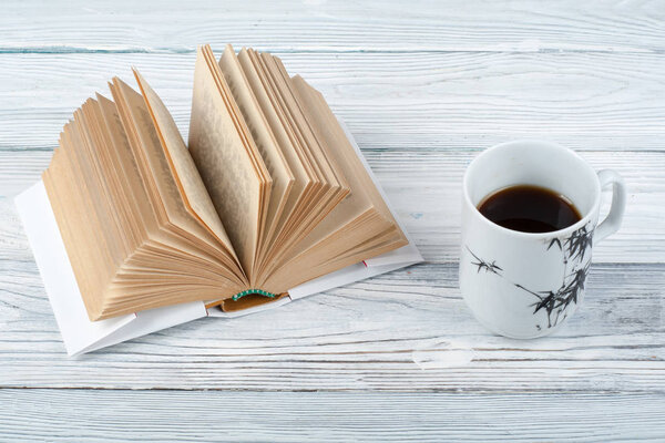 Open book, coffee cup and snack on wooden table background.