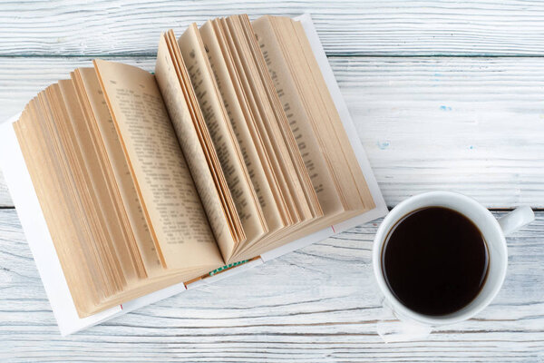 Open book, coffee cup and snack on wooden table background.