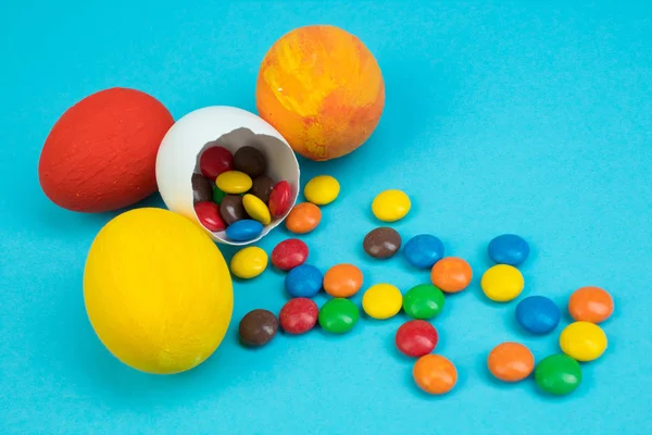 Happy Easter. Broken Easter egg with multi-colored candy decorations on blue background. Colorful eggs.