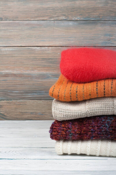 Knitted wool sweaters. Pile of knitted winter clothes on wooden background, sweaters, knitwear, space for text