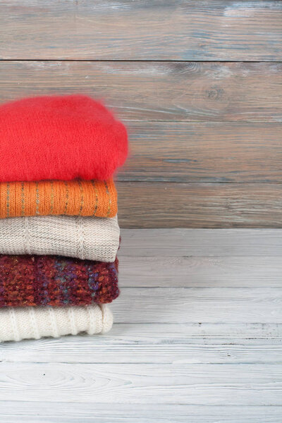 Knitted wool sweaters. Pile of knitted winter clothes on wooden background, sweaters, knitwear, space for text