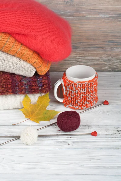 Knitted wool sweaters. Pile of knitted winter, autumn clothes on red, wooden background, sweaters, knitwear, ball, cup, leaf space for text. — Stock Photo, Image