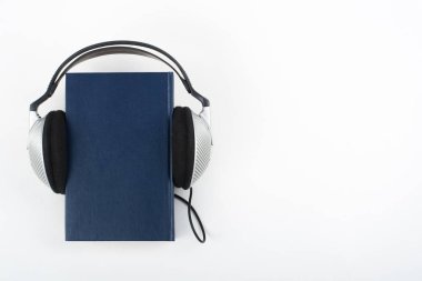 Beyaz arka planda Audiobook. Kulaklıklar mavi kaplı defter, boş kapak, reklam metni için kopyalama alanı. Uzaklık eğitimi, e-öğrenme kavramı