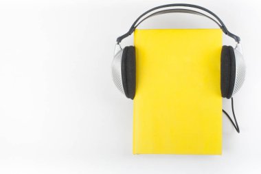 Beyaz arka planda Audiobook. Kulaklıklar sarı kaplı defter, boş kapak, reklam metinleri için kopya alanı. Uzaklık eğitimi, e-öğrenme kavramı