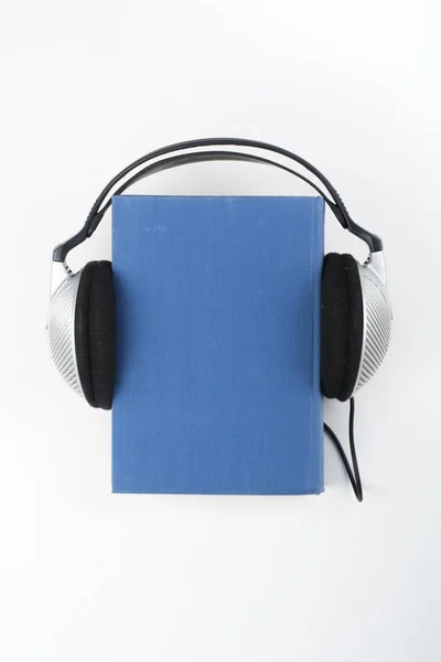 白い背景のオーディオブック ヘッドフォンは青いハードバック本 空のカバー 広告テキスト用のコピースペースを置きます 距離教育 Eラーニングの概念 — ストック写真