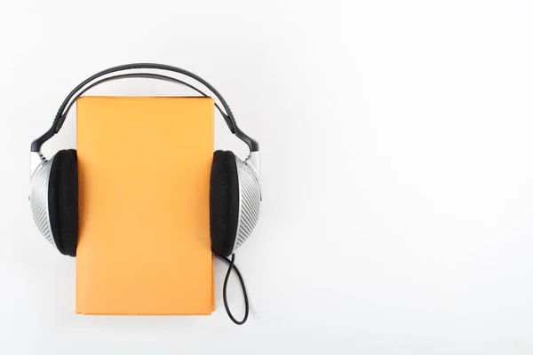 白い背景のオーディオブック ヘッドフォンは黄色のハードバックブック 空のカバー 広告テキスト用のコピースペースを置きます 距離教育 Eラーニングの概念 — ストック写真
